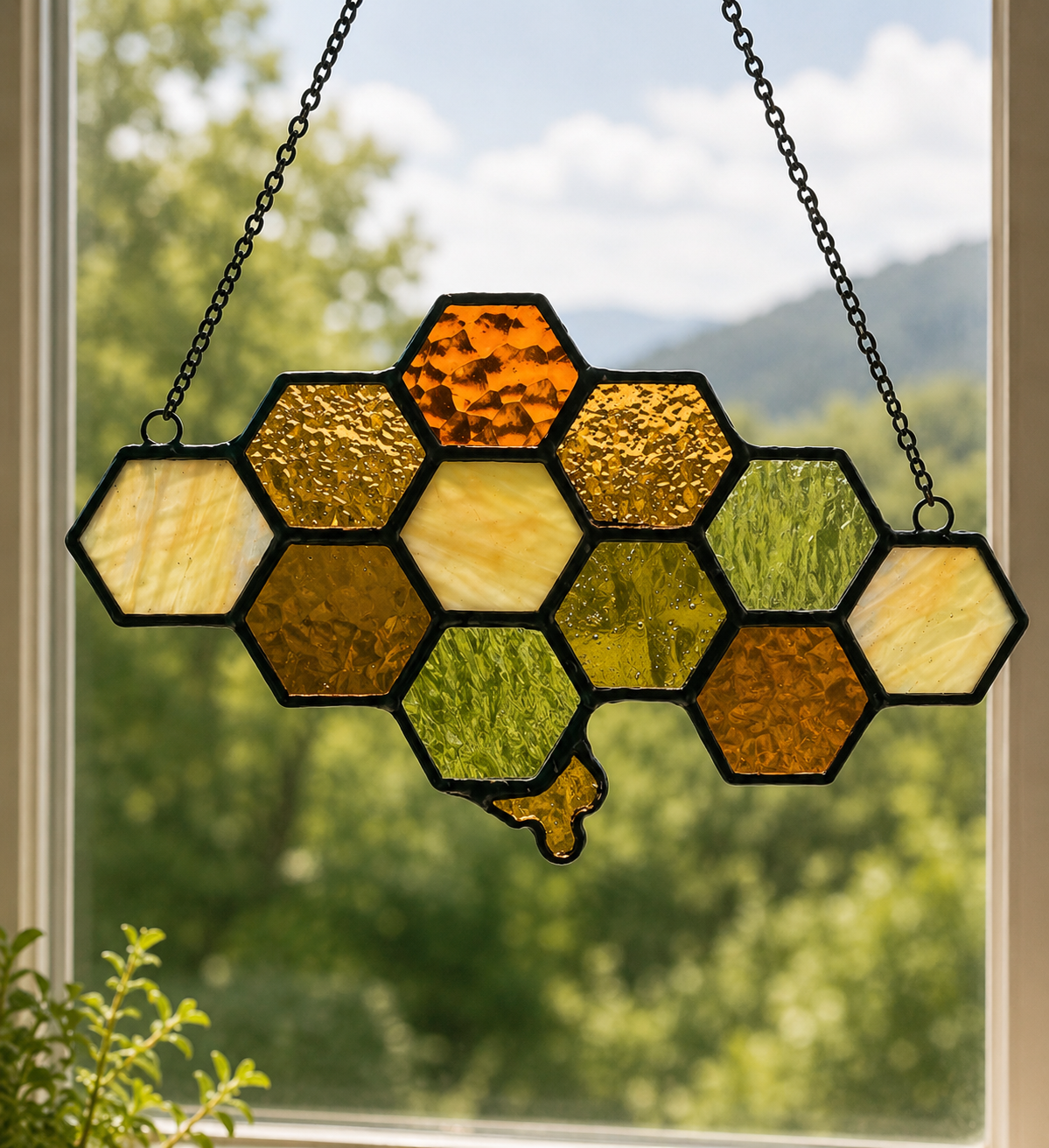 Amber, moss, and cream stained glass honeycomb suncatcher hanging in front of a green landscape.